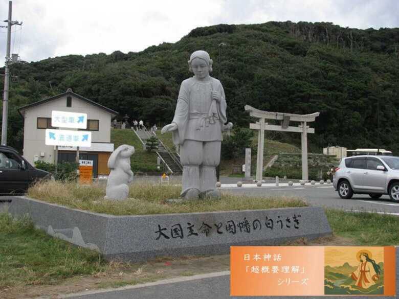 日本神話シリーズ 因幡の白兎 白兎海岸側の大国主と白兎の像。 後ろは白兎神社の鳥居。手前の舗装帯の右手に道の駅神話の里 白うさぎがある。